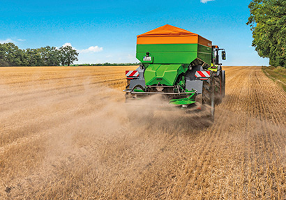 CLAAS-traktori vetää perässään Amazone XG-TX-kalkinlevytyslaitetta.