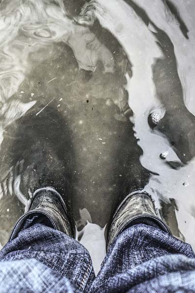 Ihminen seisoo saappaat jalassa likaisessa vedessä, jota on melkein saappaanvarteen asti.
