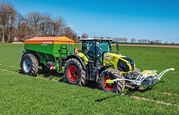 CLAAS-traktori vetää perässään Amazone XG-TX-kalkinlevytyslaitetta.