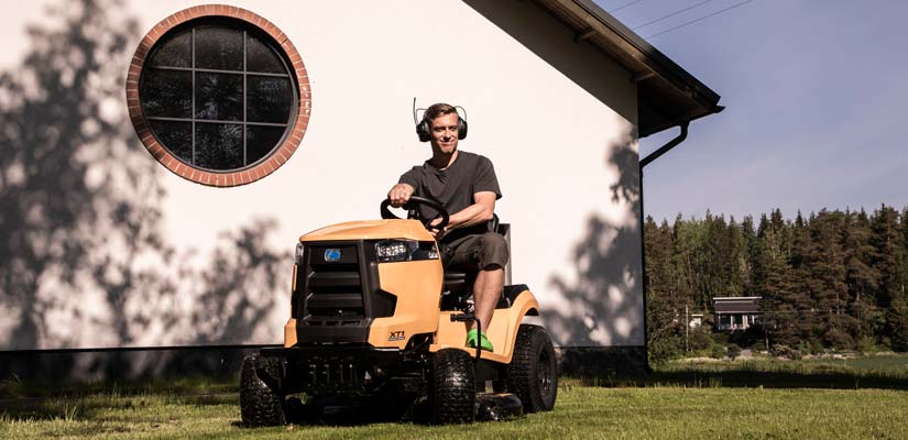 Mies ajaa päältäajettavalla ruohonleikkurilla nurmikkoa kuulokkeet päässä