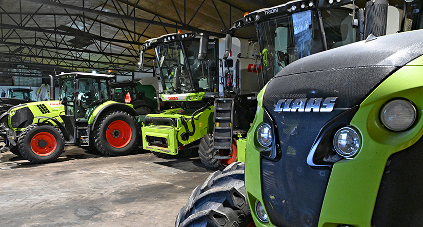 Kaksi CLAAS-traktoria ja CLAAS-leikkuupuimuria hallissa rivissä.