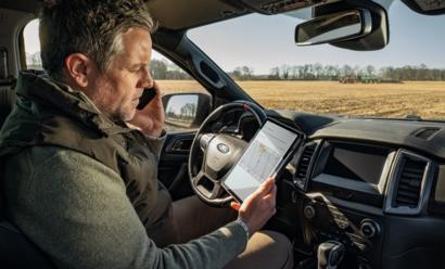CEBIS Connect -hallintalaitteiston katselua henkilöauton puikoissa. Taustalla näkyy CLAAS AXION 8 -traktori.