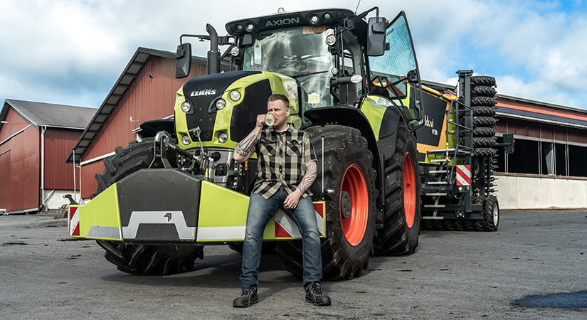 Mies nojaa tyytyväisenä CLAAS-traktorin etupainoon ja hörppii kahvia.
