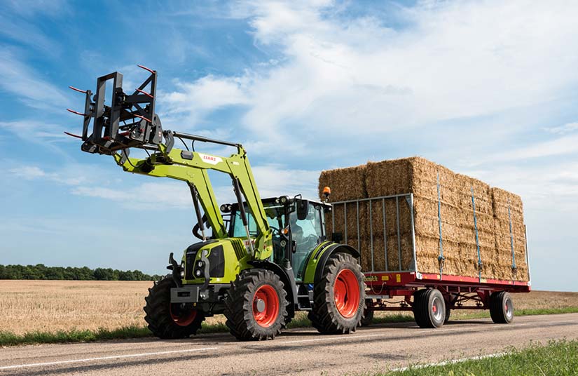 CLAAS -etukuormaaja traktorissa, joka vetää paalikuormaa tiellä.