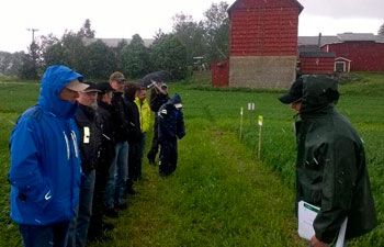 Kasvuohjelma-tilaisuuden osallistujia pellolla seuraamassa koeruutuja sateisessa säässä.