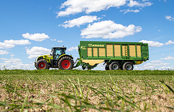 CLAAS vetää Kronen noukinvaunua keväisellä pellolla.