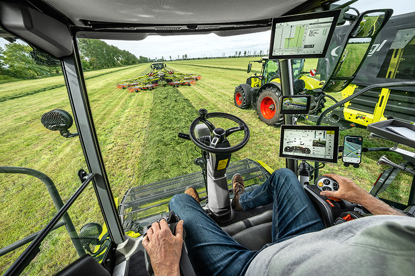 Laaja kuva Jaguarin ohjaamon näkökulmasta. Edellä ajaa Claas-traktori karhottimella, vieressä Claas-traktori Flieglin noukinvaunun kanssa.