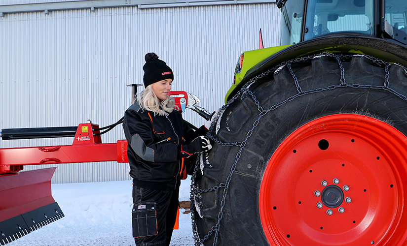 Nainen asentaa ketjuja CLAAS-traktoriin.