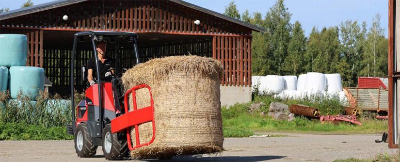 Norcar-pienkuormaaja nostelee painavaa paalia paalipihdeillä.
