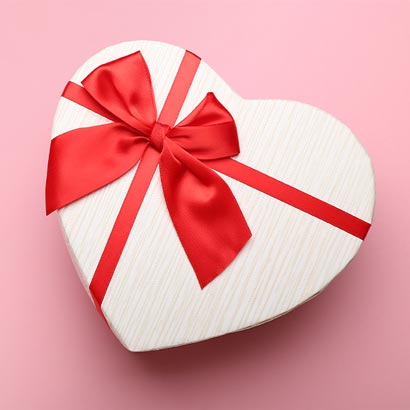 Vaaleanpunainen tausta ja sydämenmuotoinen lahjapaketti ystävänpäivään.